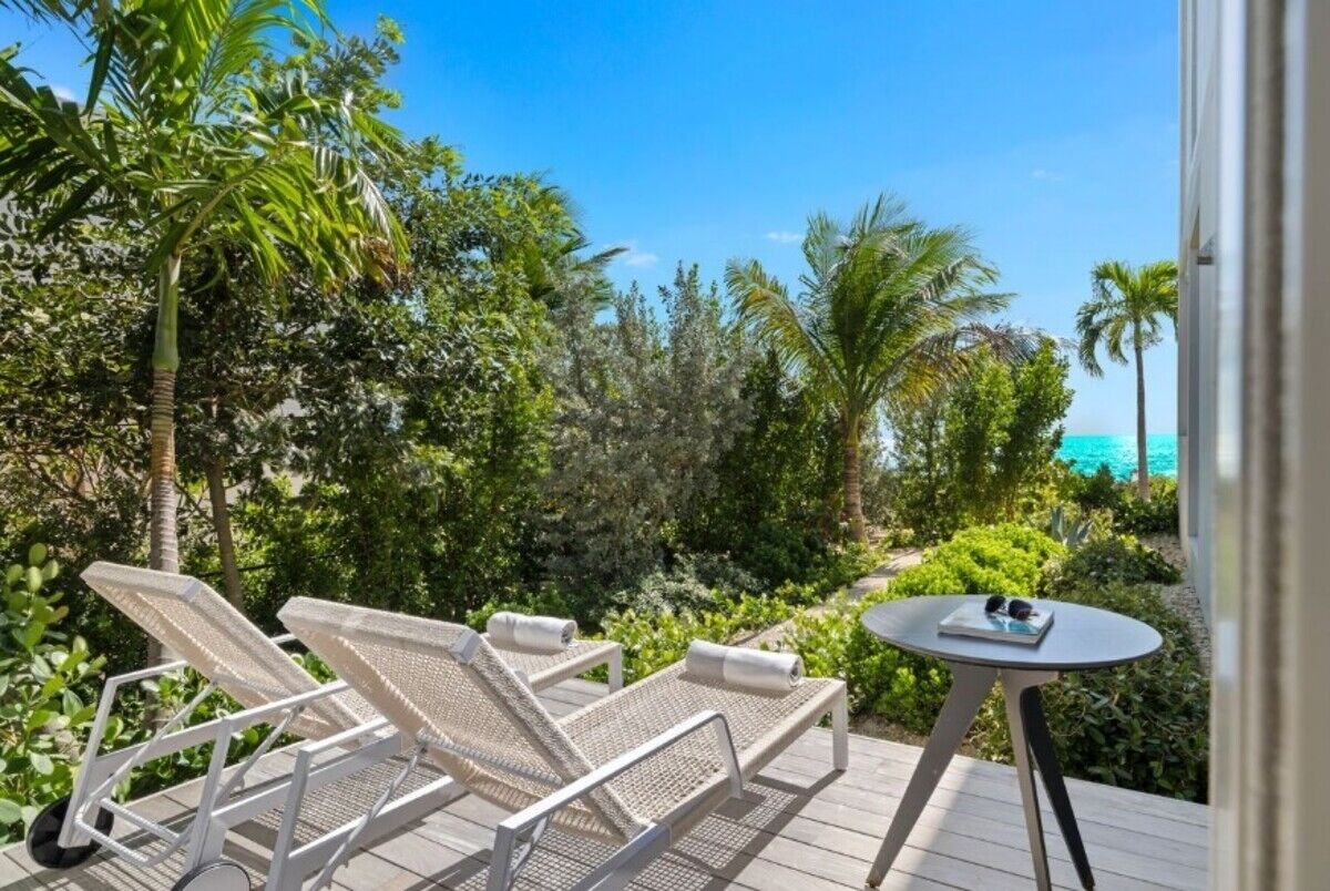 A deck with two lounge chairs and a small table, surrounded by lush greenery and overlooking a clear blue sea.