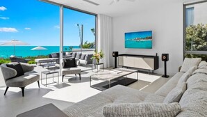 A modern living room with a large window overlooking the ocean, a flat-screen TV, and a ceiling fan. - Revitalize w/ Peaceful Balcony Views in Contemporary Island Paradise Room (Long Bay Hills)