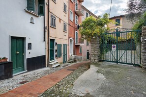 A narrow alleyway with a cobblestone path, a green gate, and a building with a stone wall and a door.