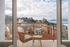 A balcony with wicker chairs and a small table, overlooking a cityscape with buildings and a distant hill. - Elegant 'Aless Views' Apartment with Sea View, Wi-Fi, and Air Conditioning (Lerici)