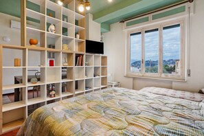 Une chambre avec un lit, un téléviseur posé sur une étagère et une fenêtre donnant sur un beau paysage.