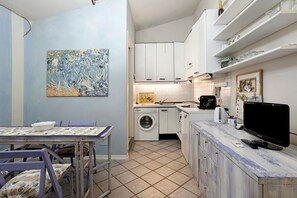 Una cocina compacta con lavadora, una mesa de comedor con sillas y un televisor.