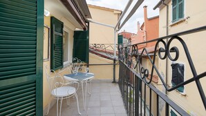 A balcony with a table and chairs, a metal railing, and a building with green shutters. - Apartment 'Piccolo Golfo' with Balcony, Wi-Fi and Air Conditioning (Lerici)