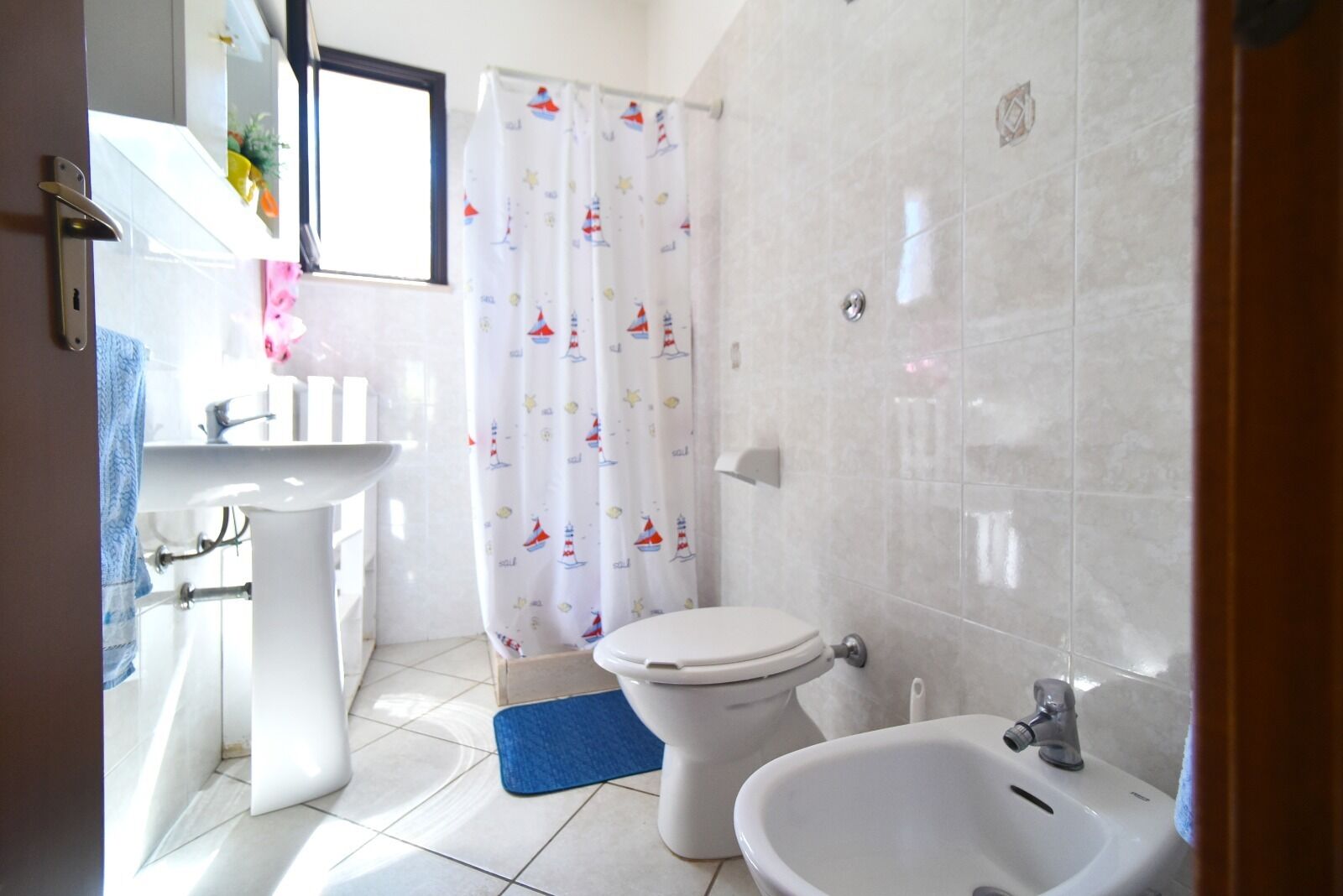 Un baño con inodoro, bidé, lavabo y cortina de ducha con motivos náuticos.