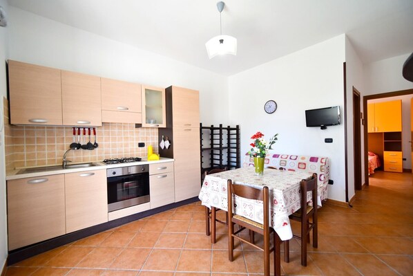 A compact kitchen with a dining table, a clock, and a TV mounted on the wall. - Piccolo Residence Gallipoli (Gallipoli)