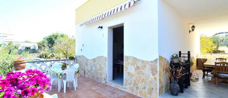 A patio with a table and chairs, a stone wall, and a building with a yellow awning.