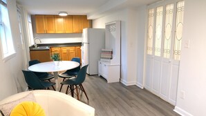 A modern kitchen with wooden cabinets, a white refrigerator, and a dining area with a white table and chairs. - Charming Getaway! Heart of Asheville Suite (Asheville)