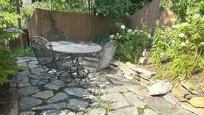 A stone patio with a round metal table and chairs, surrounded by a wooden fence and greenery. - Charming Getaway! Heart of Asheville Suite (Asheville)