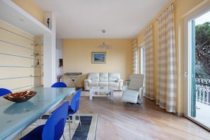 Una sala de estar con sofá, sillón, mesa de centro de vidrio y una mesa de comedor con sillas.