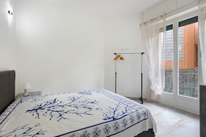 Ein Schlafzimmer mit einem Bett, einem Nachttisch, einem Fenster mit Vorhängen und Blick ins Freie.