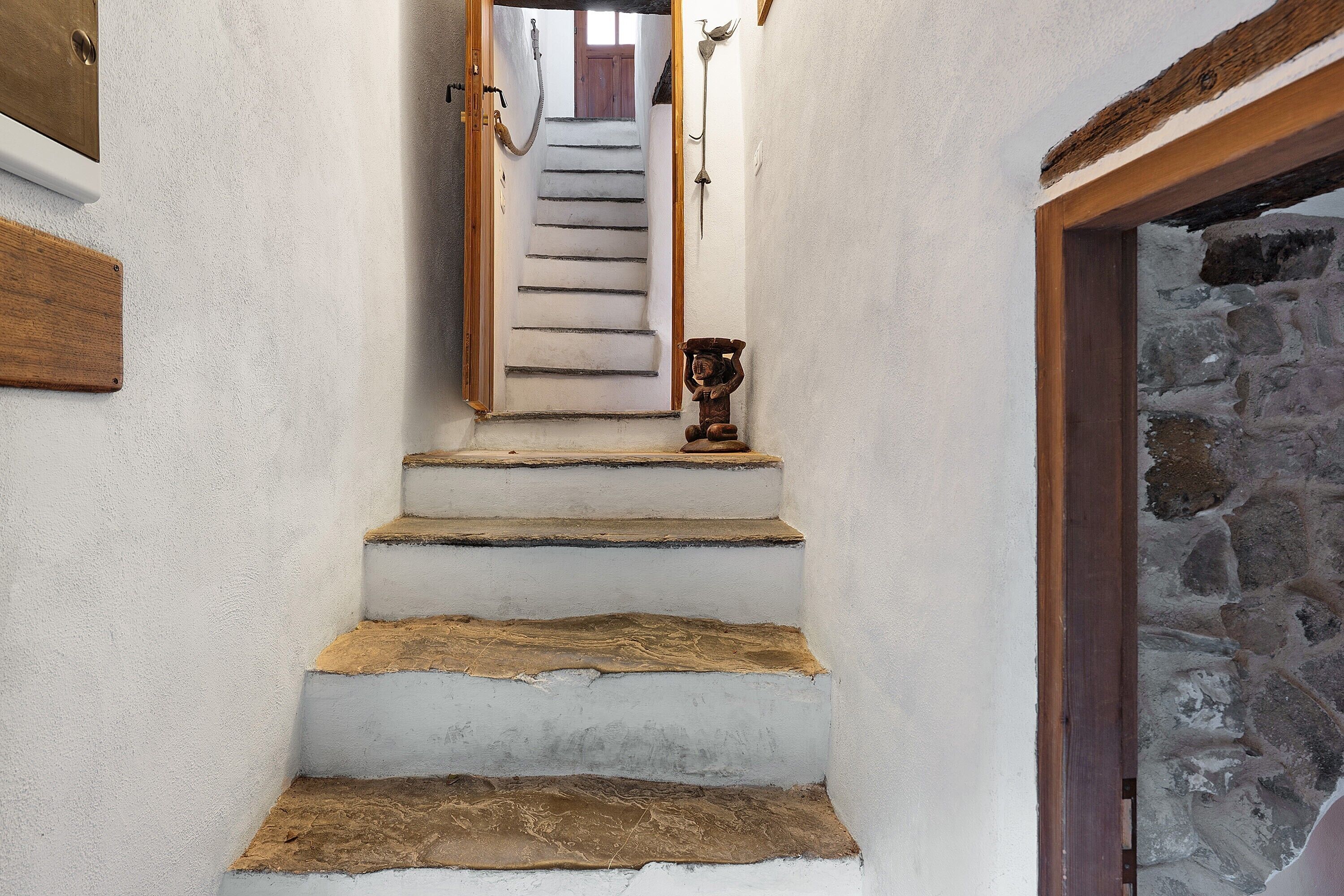 Un escalier aux murs blancs, avec une main courante en bois et un mur en pierre au bas.