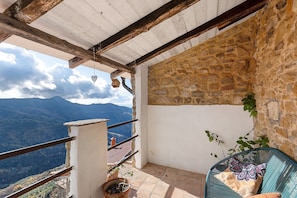 A balcony with stone walls, a view of mountains, and a potted plant.