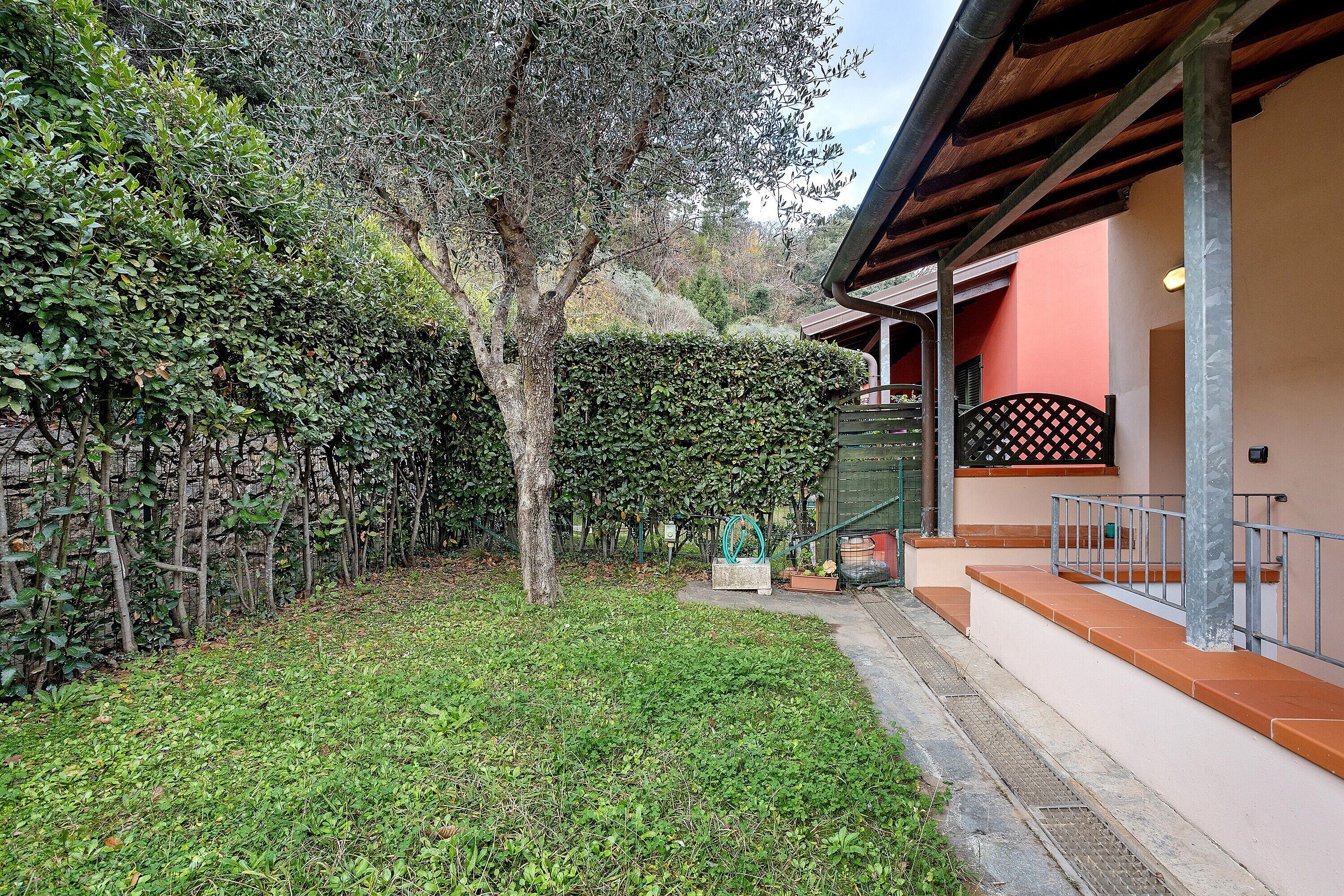 A courtyard with a tree, a fence, and a building with a red wall and a balcony.