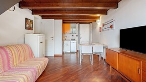 Una habitación con sofá, una mesa de comedor con sillas, televisión y cocina al fondo.
