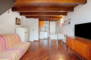 Una habitación con sofá, una mesa de comedor con sillas, televisión y cocina al fondo.