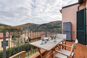 A balcony with a table set for two, a view of the surrounding landscape, and a building with a green shutter. - Apartment 'Lerici – Foyer Verde Mare' with Mountain View, Wi-Fi and Air Conditioning (Lerici SP)