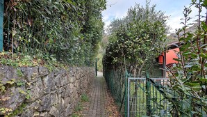 Un estrecho sendero de piedra bordeado por una vegetación densa y una puerta de metal.