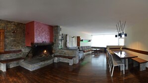 Ein geräumiges Wohnzimmer mit Kamin aus Stein, einer Essecke mit langem Tisch und Stühlen sowie einer Steinsitzbank.