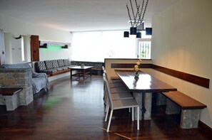 A spacious living area with a stone accent wall, a wooden bench, a dining table, and a hanging light fixture.
