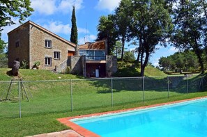 A stone house with a swimming pool, surrounded by a fence and trees.
