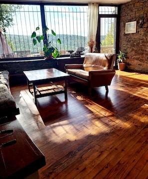 A room with a wooden floor, a sofa, a coffee table, and a view through large windows.