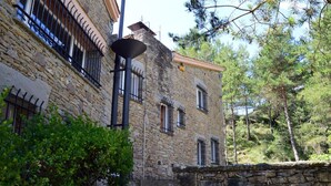 Ein Steinhaus mit vergitterten Fenstern, einer Steinsäule und einer Treppe, die zum Eingang führt.