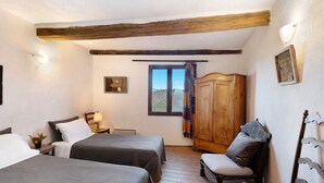 Een kamer met twee bedden, een houten garderobe, een stoel, een raam met gordijnen en een wandlamp.