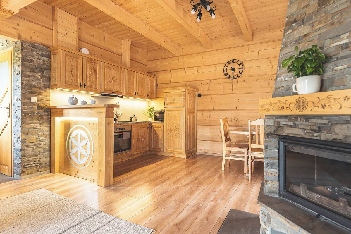 A wooden cabin interior with a stone fireplace, wooden cabinets, and a stone wall.