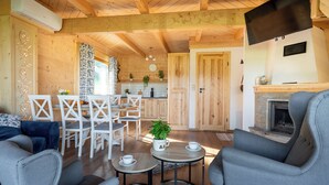Un salon chaleureux avec une cheminée, un coin repas avec une table et des chaises, et une cuisine en arrière-plan.