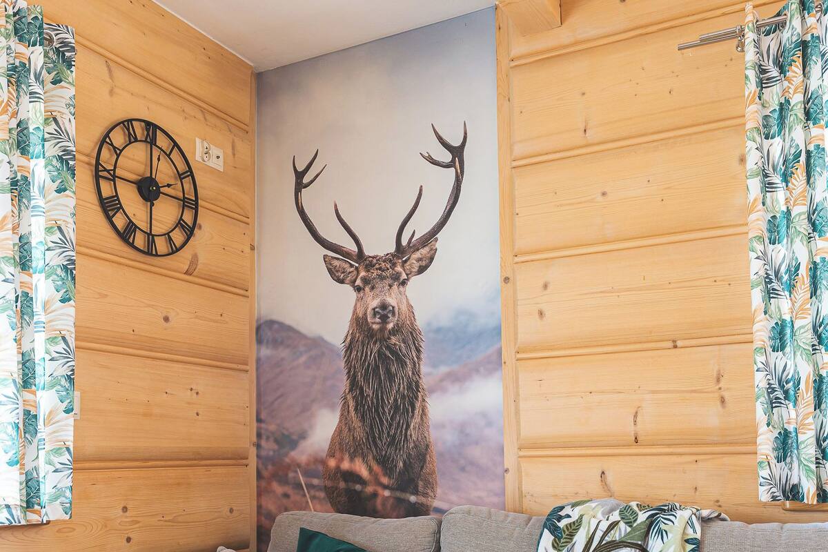 A cozy cabin interior with a large sectional sofa, a wall clock, and a deer mural.