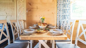 Une table de salle à manger en bois, mise avec des assiettes, des bols et une salade, entourée de chaises blanches dotées de coussins gris.