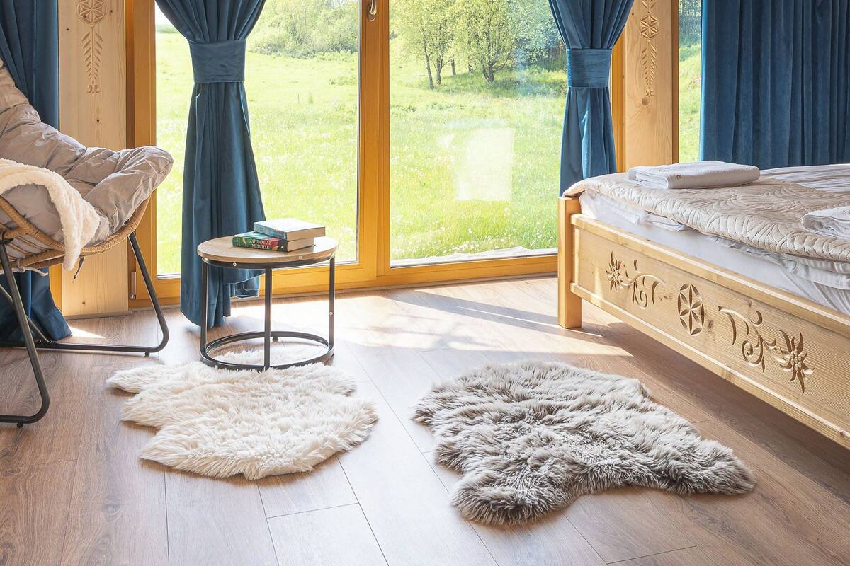 A bedroom with a large window, a bed, a chair, and a small table.