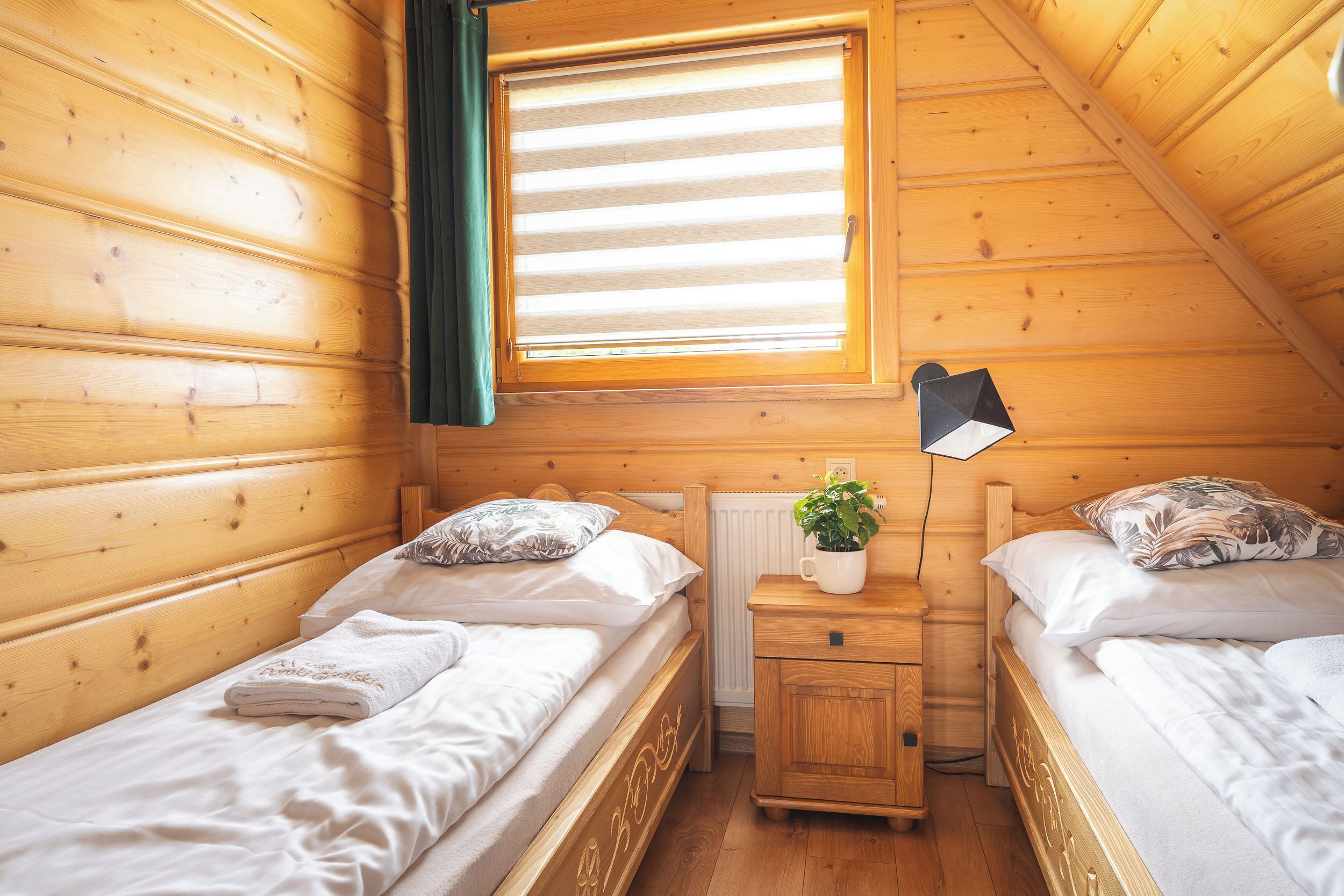 Une chambre confortable dans un chalet, avec deux lits en bois, une table de chevet avec une lampe et une fenêtre équipée de stores.