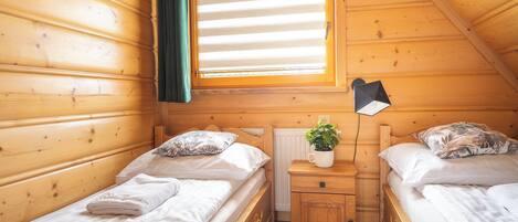 Une chambre confortable dans un chalet, avec deux lits en bois, une table de chevet avec une lampe et une fenêtre équipée de stores.