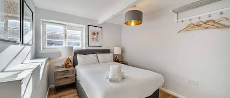 Un dormitorio ordenado con cama, mesitas de noche, una lámpara colgante y una ventana.