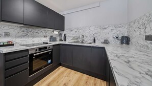 Una cuina moderna amb armaris foscos, taulell de marbre i forn integrat.