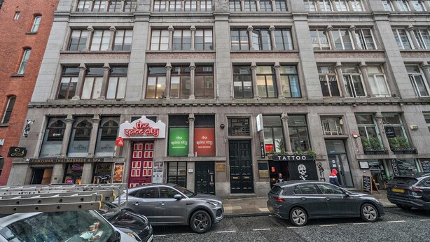 Ein mehrstöckiges Gebäude mit verschiedenen Geschäften im Erdgeschoss, darunter ein Massagestudio und Spa, ein Restaurant und ein Tätowierstudio.