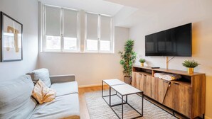 Ein modernes Wohnzimmer mit einer Couch, einem Couchtisch, einem Fernseher und einem Fenster mit Jalousien.