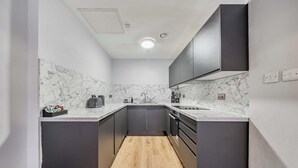 A compact kitchen with dark cabinets, a marble backsplash, and a wooden floor. - Host Stay Apartment 5 Stanley Street (Liverpool)