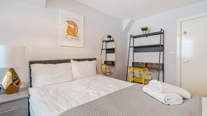 A bedroom with a bed, a bedside table, a lamp, a mirror, a shelf with a plant, and a door. - Host Stay Apartment 10 Stanley Street (Liverpool)