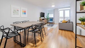 A modern living room with a wooden dining table, black chairs, a grey sofa, and a television. - Host Stay Apartment 10 Stanley Street (Liverpool)