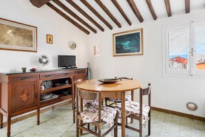 Un coin repas avec une table et des chaises en bois, un téléviseur et une fenêtre donnant sur des immeubles.