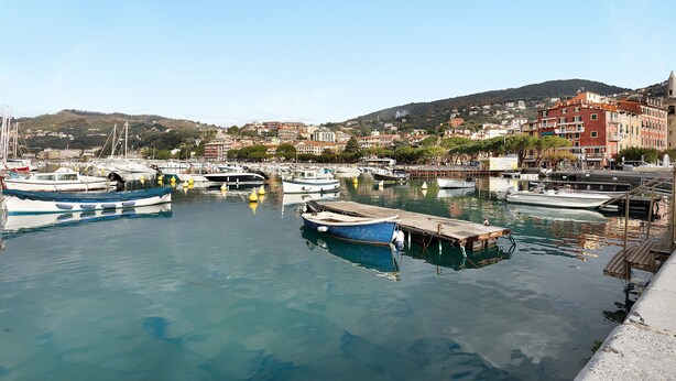 Una marina con barcos amarrados, un muelle y edificios al fondo.