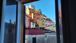 Vista a través de una ventana que muestra edificios coloridos, cielo despejado y un muro rojo.