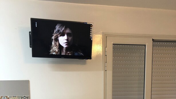 Eine kompakte Küchenzeile mit Kühlschrank, einer kleinen Arbeitsfläche und einem an der Wand befestigten Fernseher.