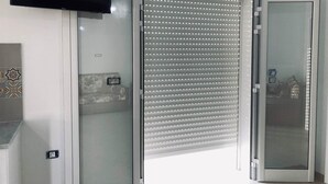 Ein Zimmer mit einer Schiebetür aus Glas, einem an der Wand befestigten Flachbildfernseher und einer wandumschließenden Küchenzeile mit gemusterten Fliesen.