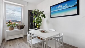 A dining area with a white table and chairs, a potted plant, a bookshelf, and a framed picture of a beach. - Apartment '5 Terre - Lerici - La Caletta' with Sea View, Wi-Fi and Air Conditioning (Lerici)
