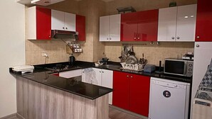 Una cucina compatta con pensili rossi e bianchi, un piano di lavoro nero, un forno a microonde integrato e una lavastoviglie.