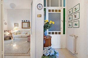 Een gang met een witte deur, een radiator en lijstwerken met botanische afbeeldingen aan de muur.
