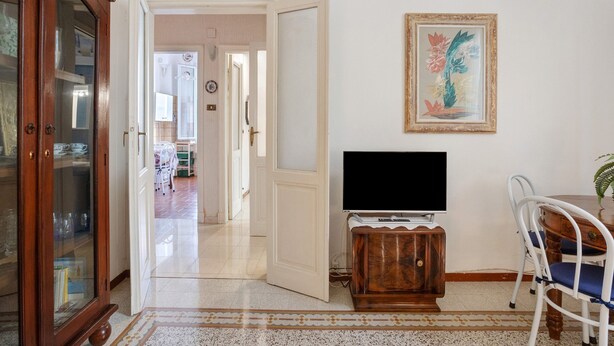 Ein Zimmer mit Fernseher auf einem Holzboden, einem Esstisch mit Stühlen und einem Schrank mit Glastüren.